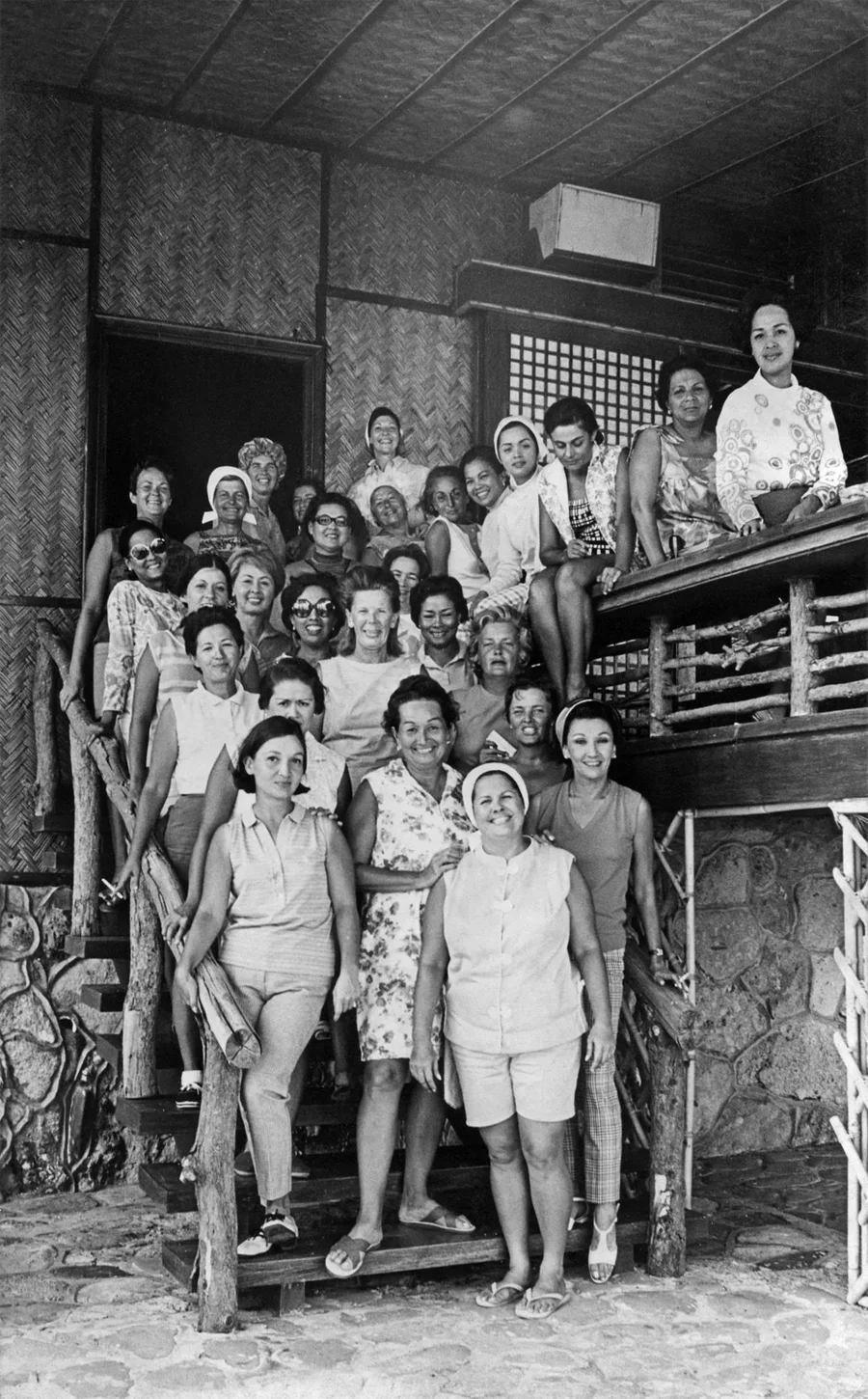 An archival black-and-white photograph of women gathered on the steps of an island house.