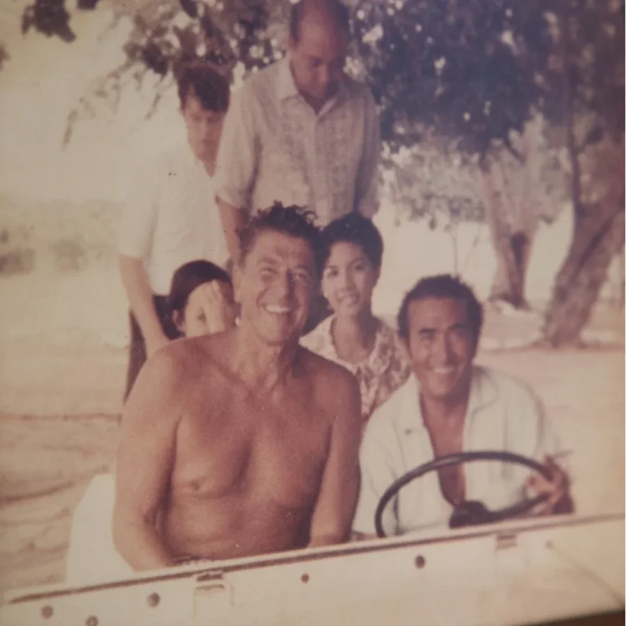 Ronald Reagan and Benigno Toda Jr. seated together in an open vehicle, with guests behind them on Hermana Mayor.