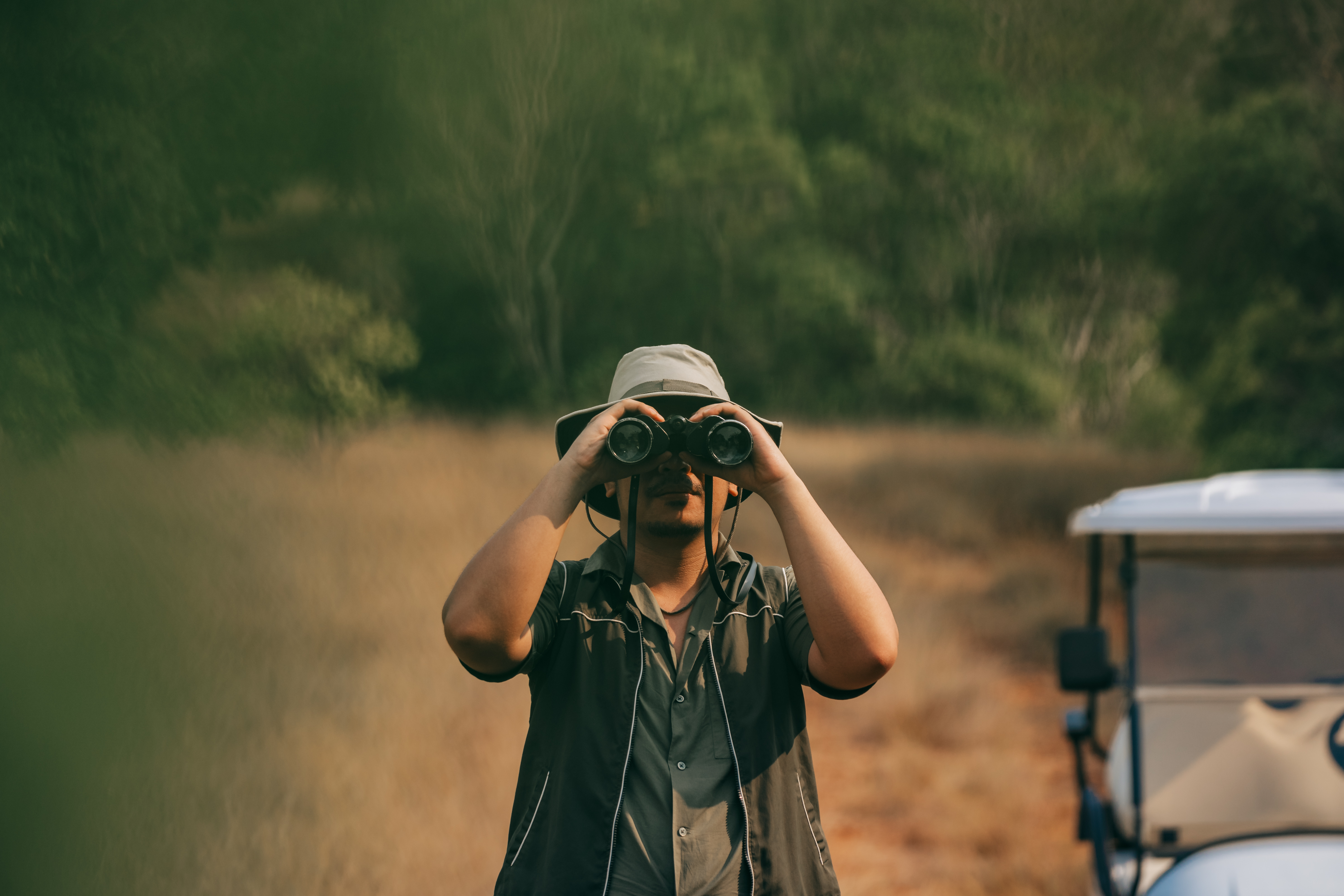 A visitor in a sun hat watches through binoculars beside an island trail.