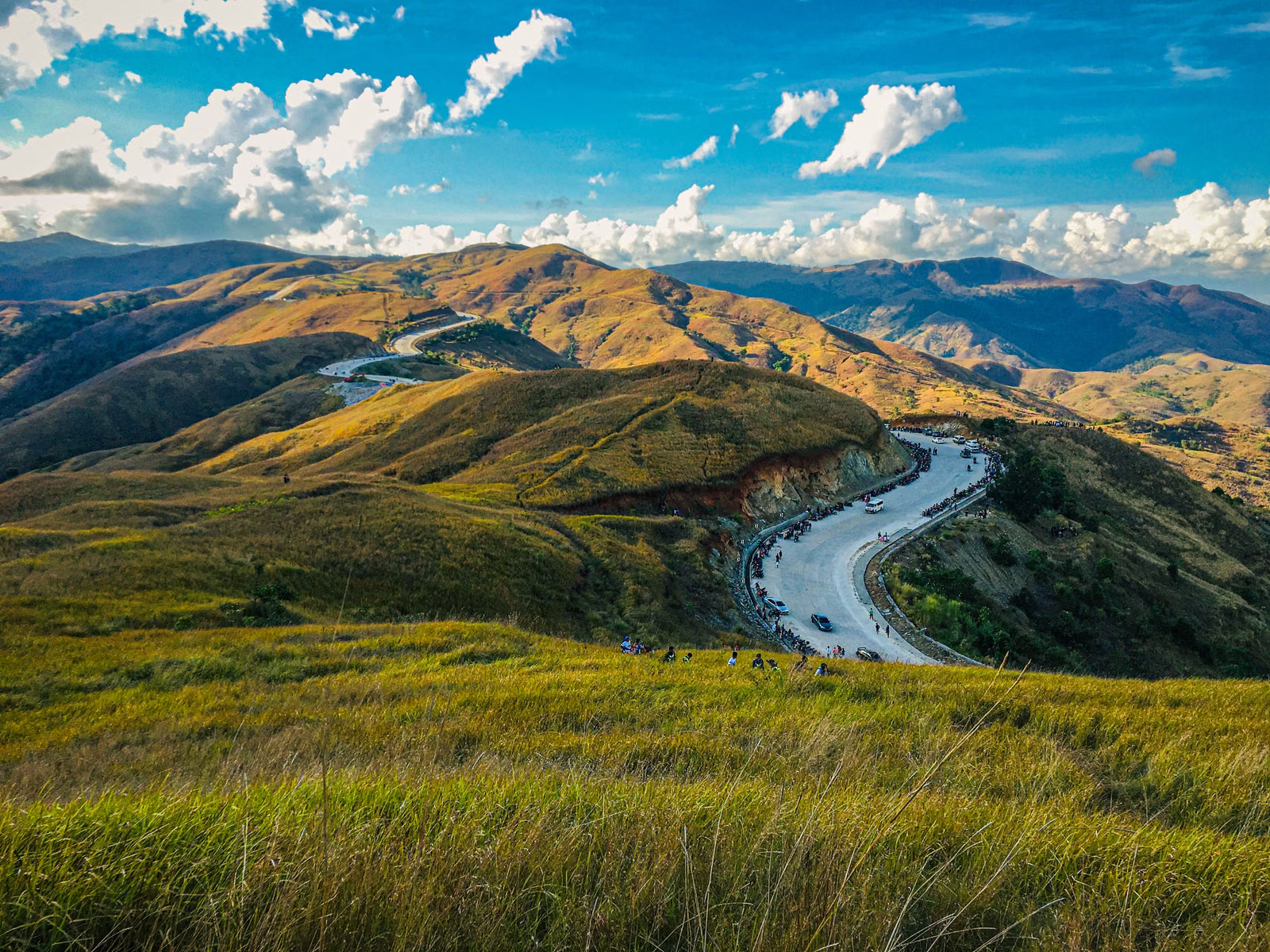 Daang Kalikasan curves through grassy mountains near Mangatarem beneath a blue sky, photographed in 2020.