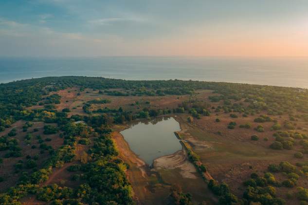 An aerial view of the island lake surrounded by woodland and open grass, with the sea beyond.